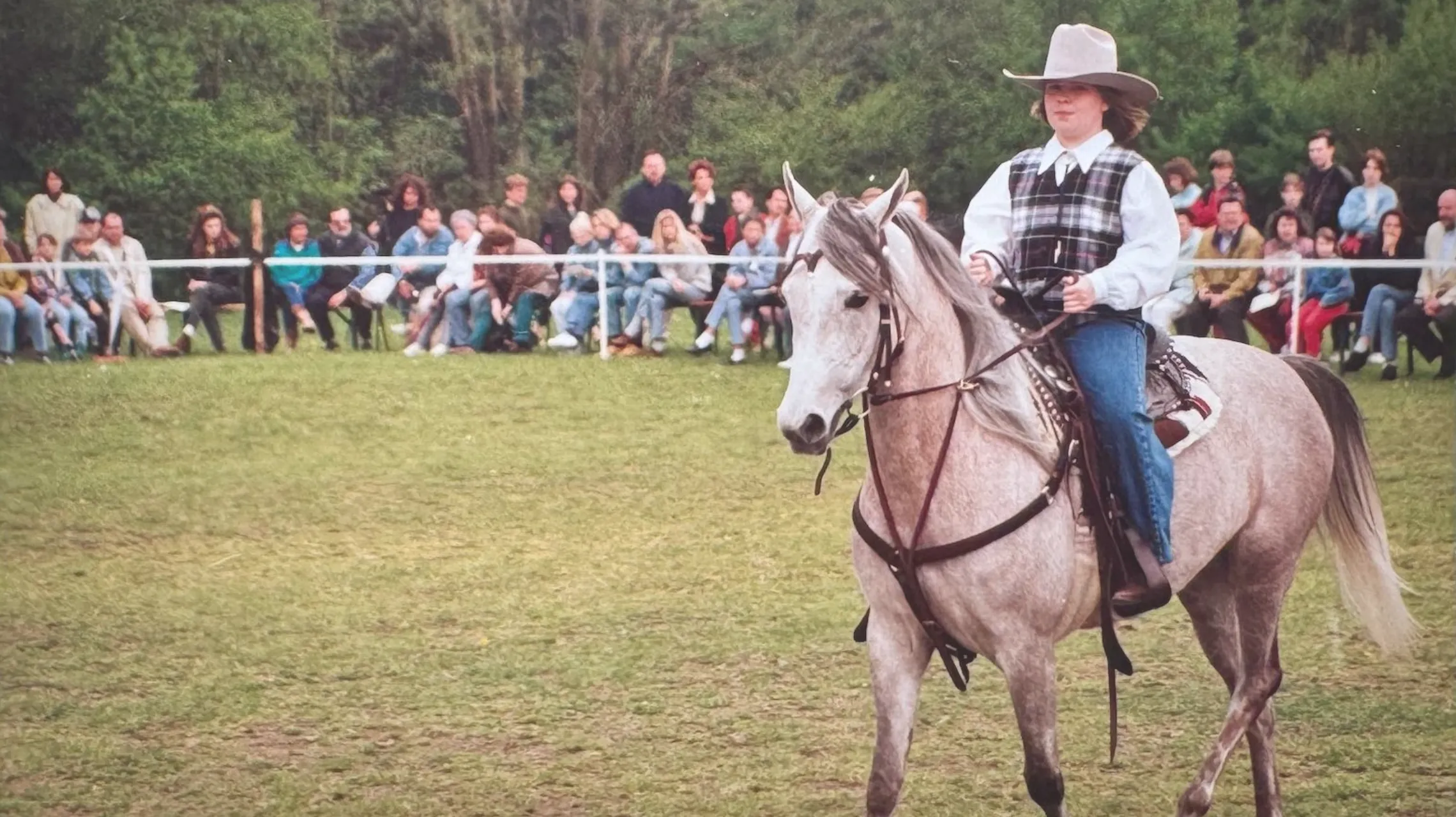 Die junge Babsi im Cowboyhut und karierter Weste reitet die Schimmelstute Chaakirah bei einem Turnier vor Publikum.