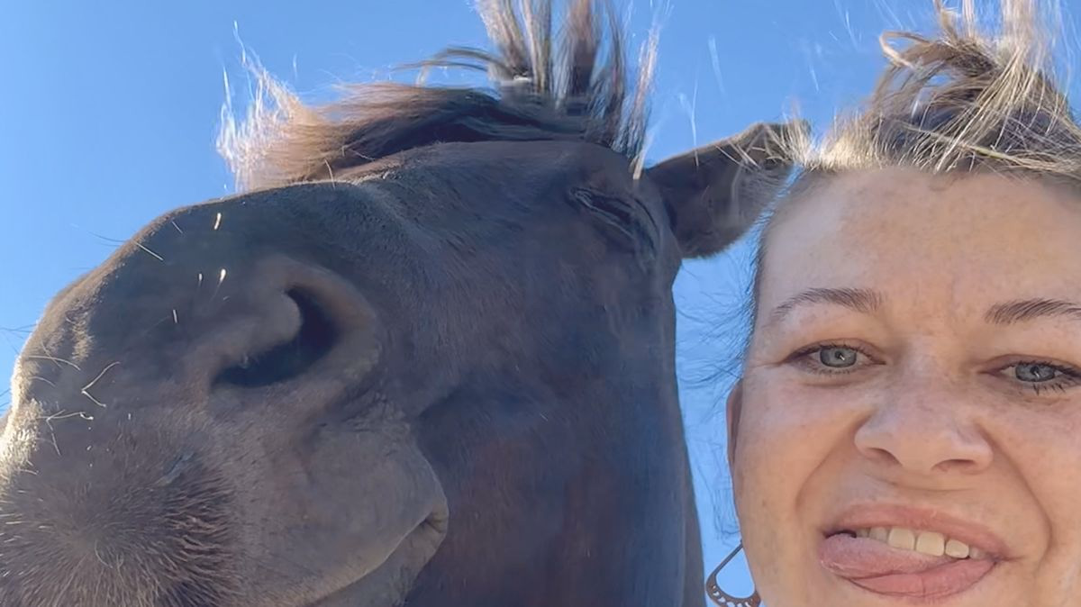 Babsi macht ein Selfie, Wange an Wange mit ihrem dunklen Pferd Franky unter blauem Himmel.
